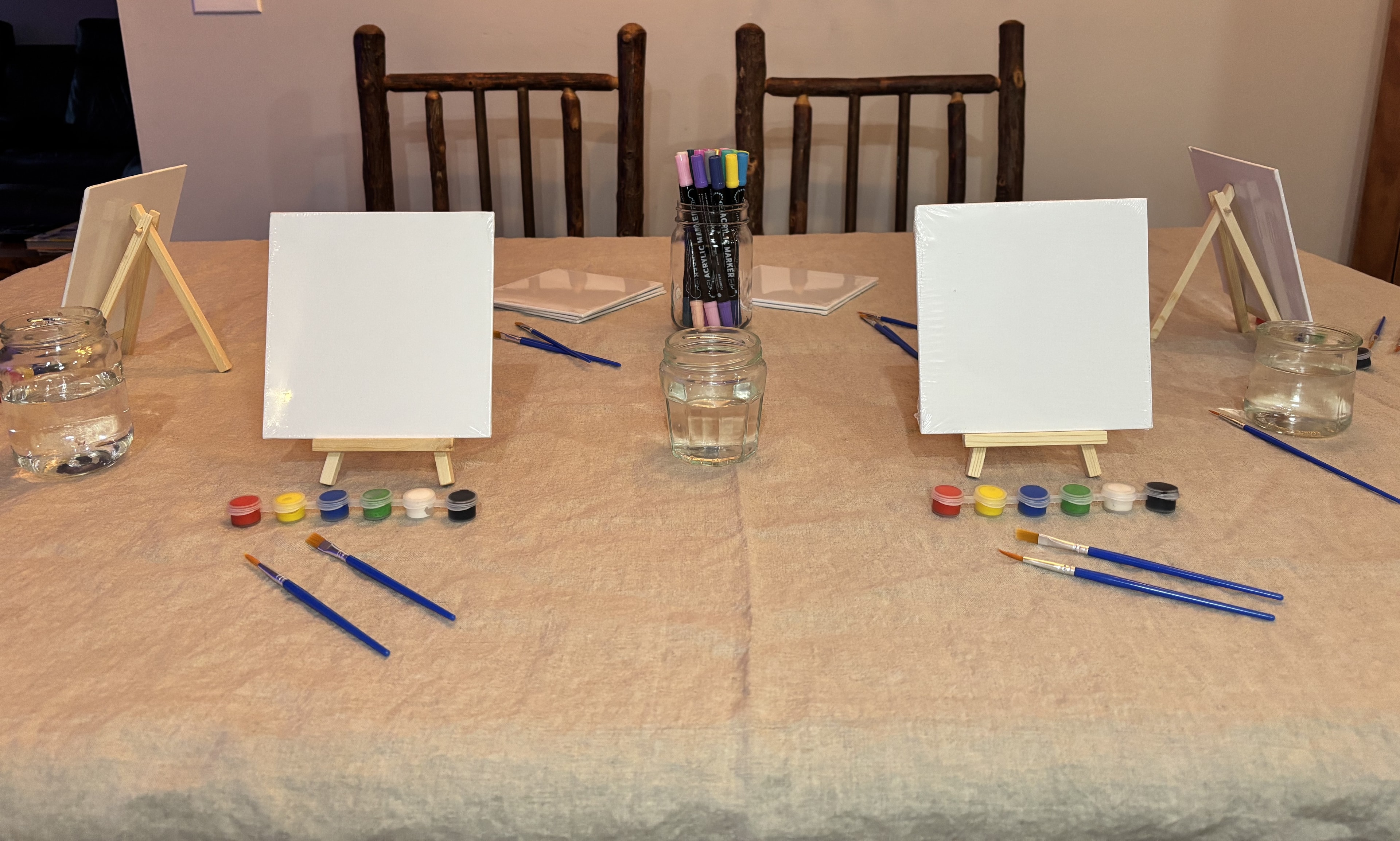 Art lesson setup with blank canvases on easels, paint pots, and brushes on a table