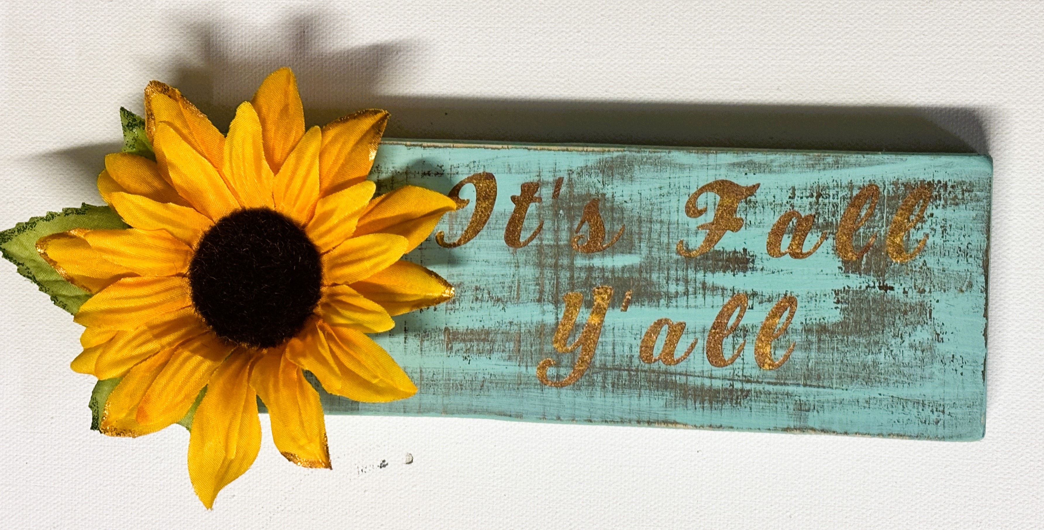 Rustic turquoise wood sign reading It's Fall Y'all with a sunflower decoration