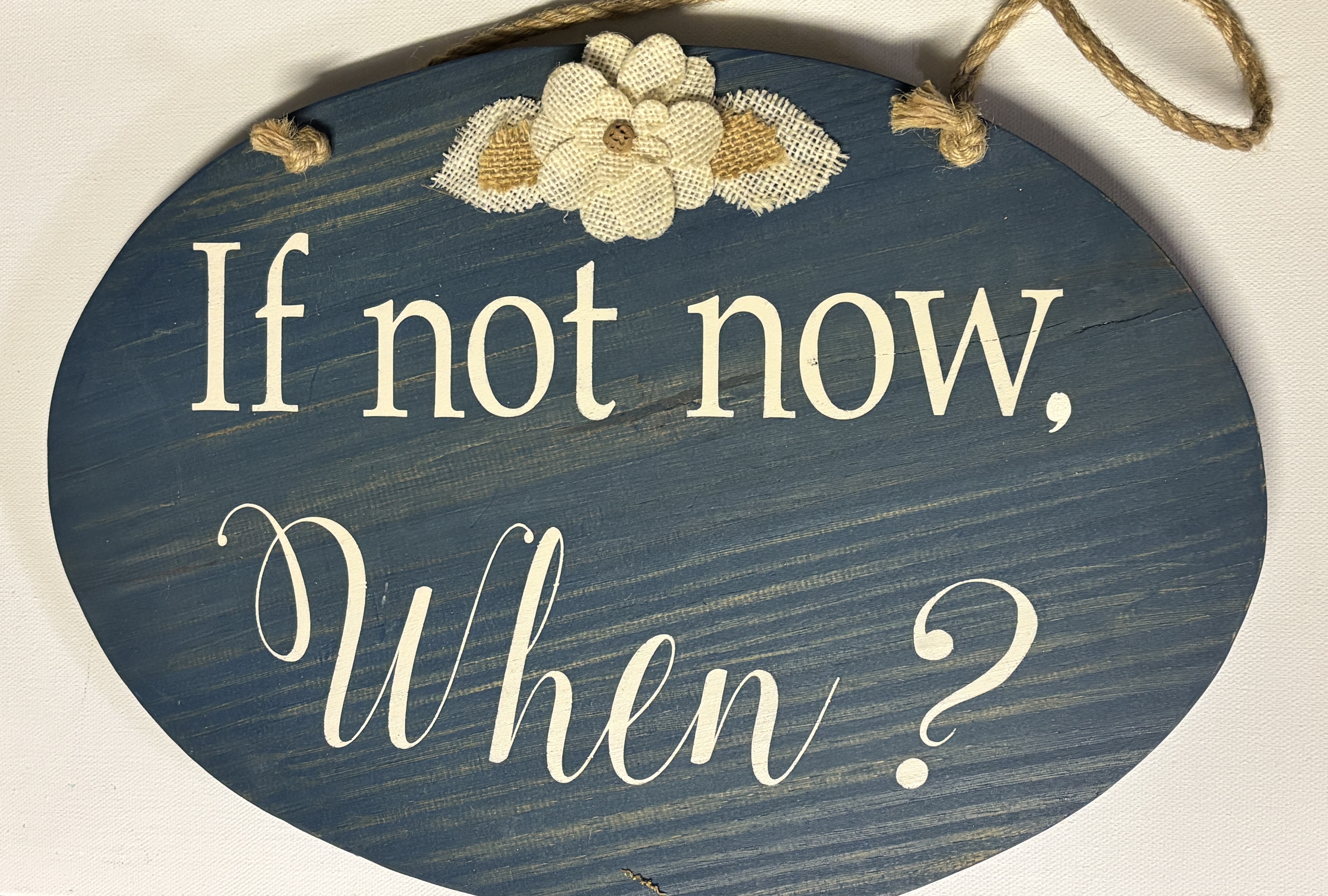 Blue oval wooden sign reading If not now, When? with burlap flower embellishment